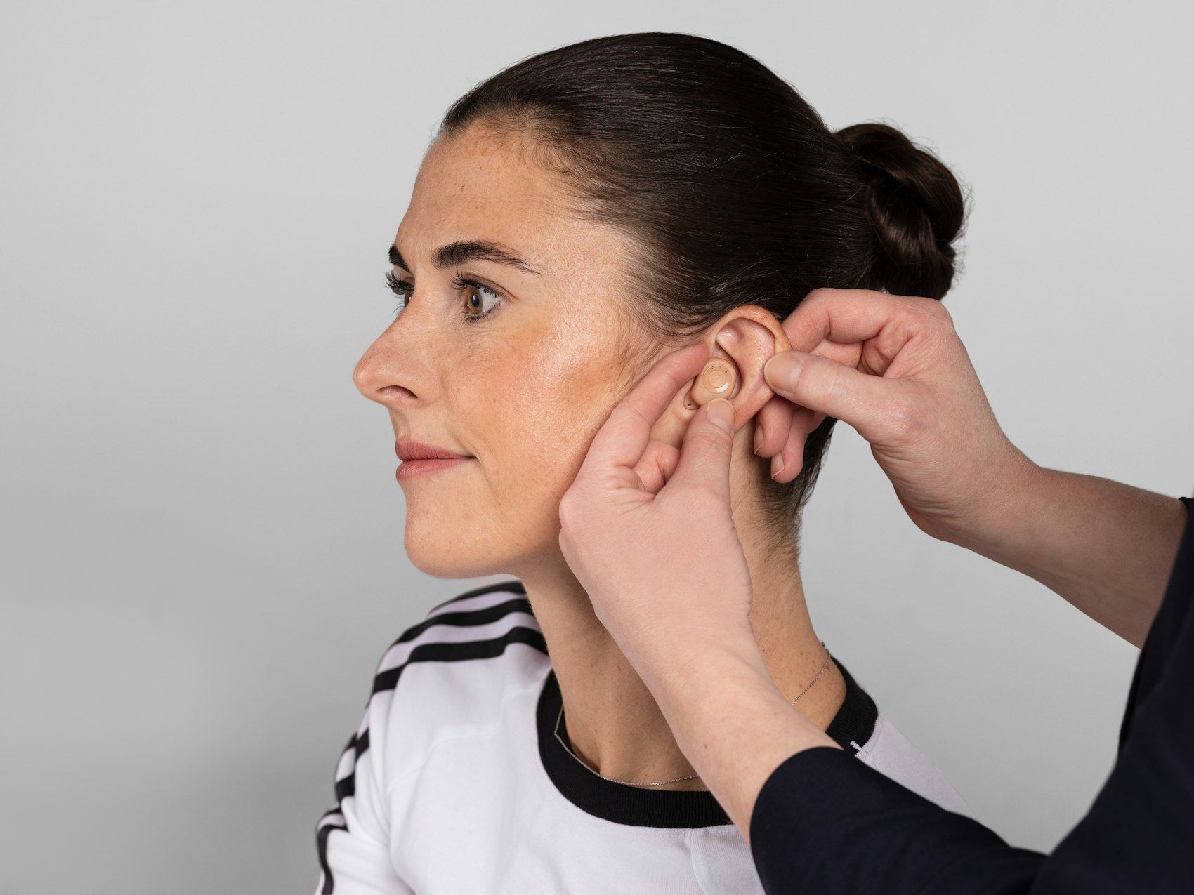 Hands fitting a hearing aid on a young woman's ear