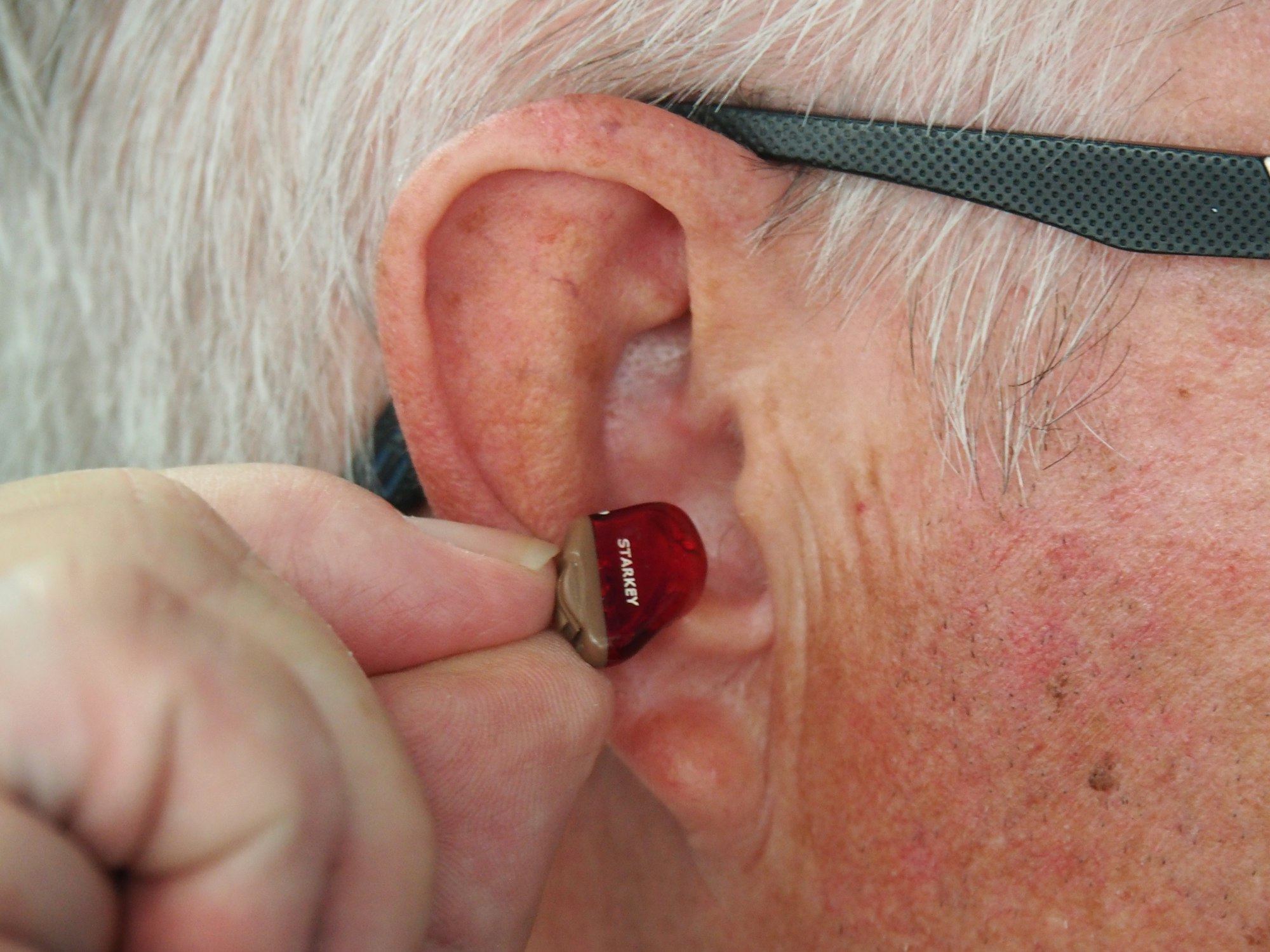 A hand inserting a red hearing aid into an ear
