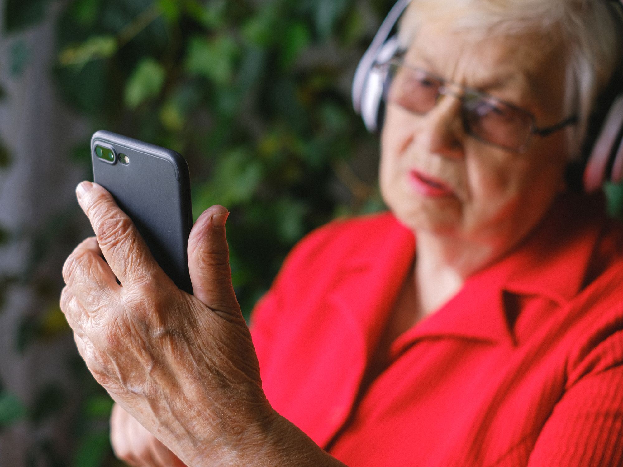 An elderly woman using a smartphone with headphones outdoors