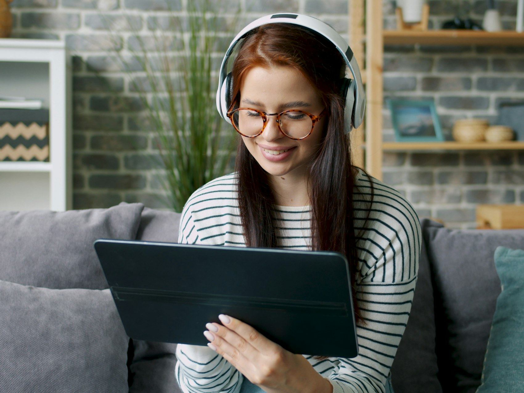Young woman wearing headphones using a tablet on a sofa