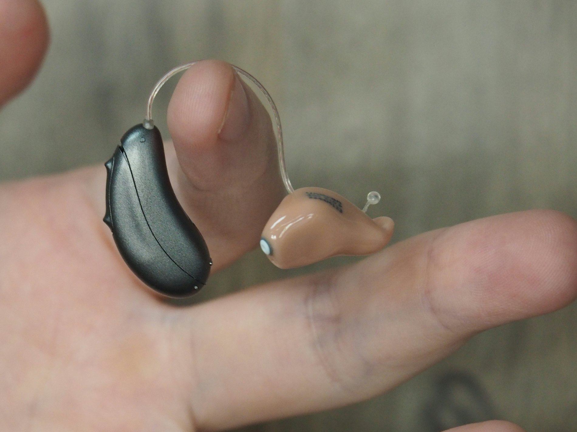 Close-up of two hearing aids held on a person's fingers